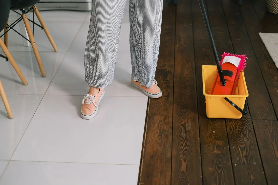 Person mopping a wet floor with a mop and bucket