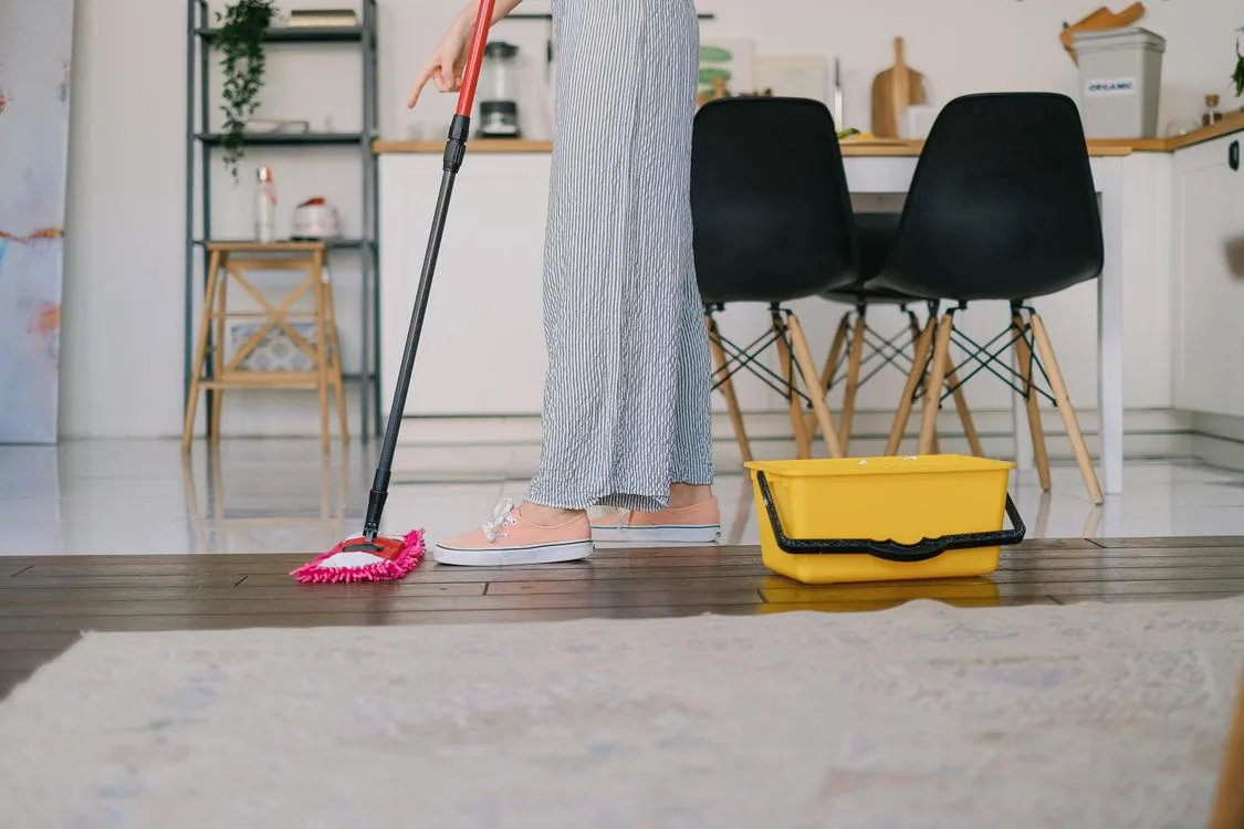 Person cleaning a wet kitchen floor with a mop and bucket